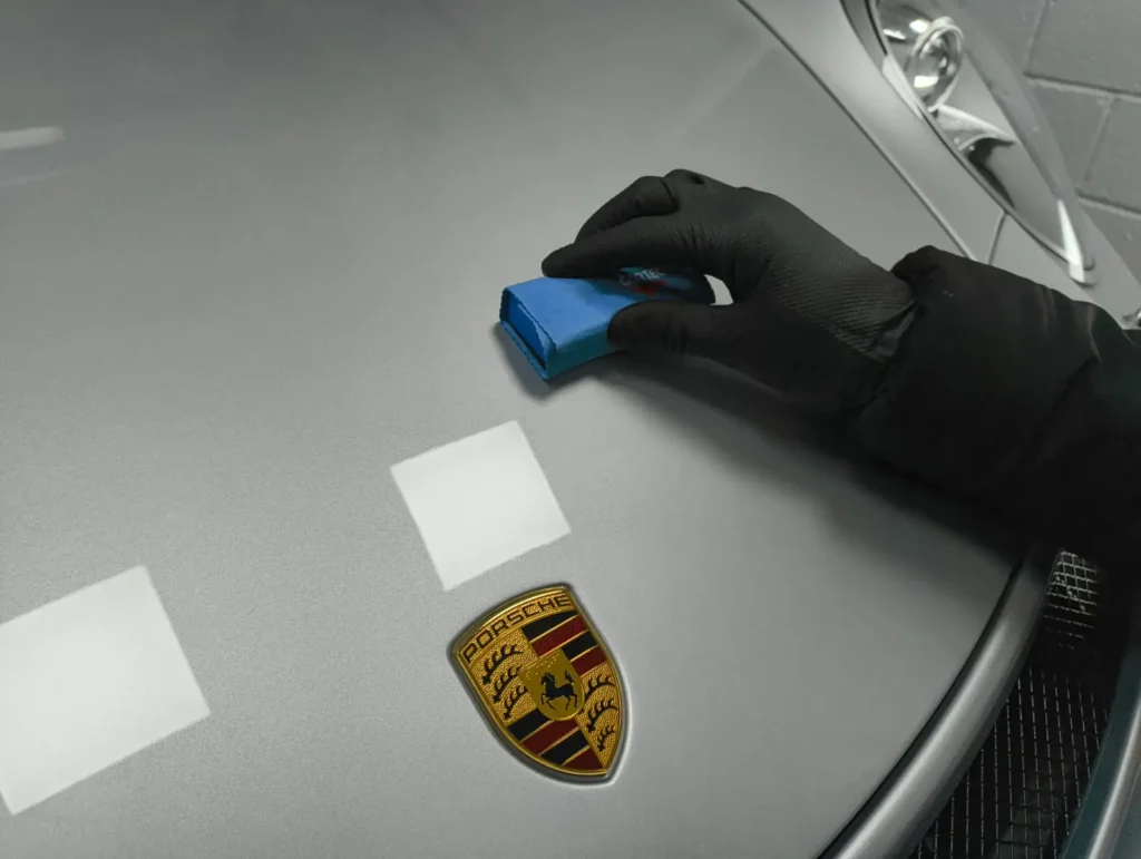 Hand wearing black glove applying ceramic coating to porsche bonnet.